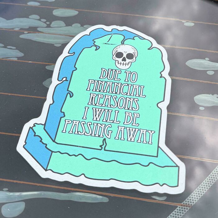Funny tombstone bumper stickers on a car window with humorous text about finances.
