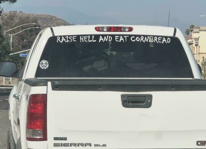 White truck with bumper stickers decal saying Raise Hell And Eat Cornbread on the rear window.