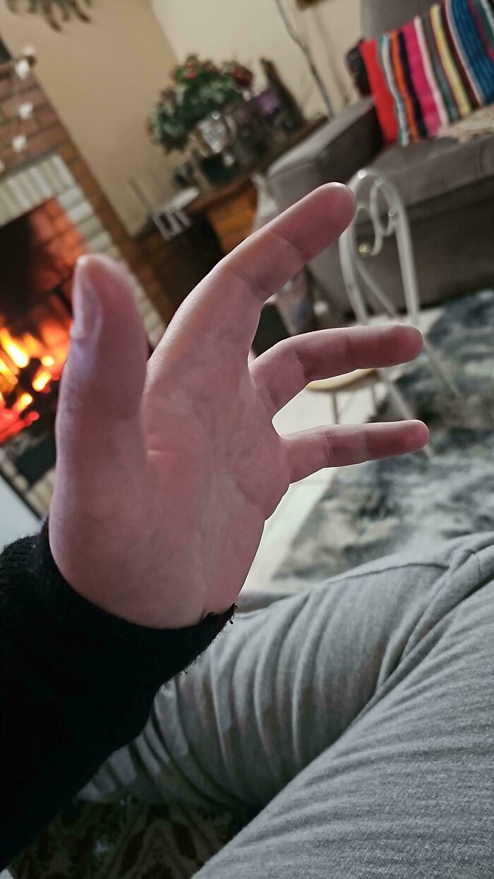 Close-up of a hand with five fingers in front of a cozy living room and fireplace