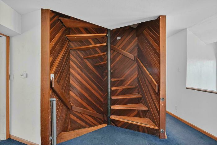 Wooden spiral staircase blending into paneled wall in an indoor setting