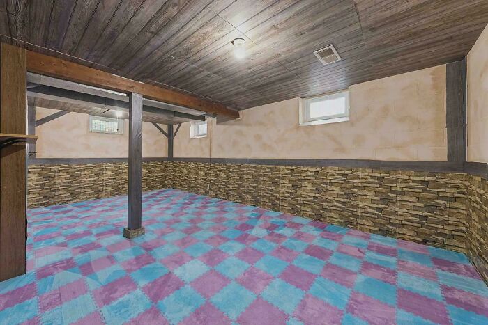 Empty basement room with colorful checkered carpet and stone-themed wall design