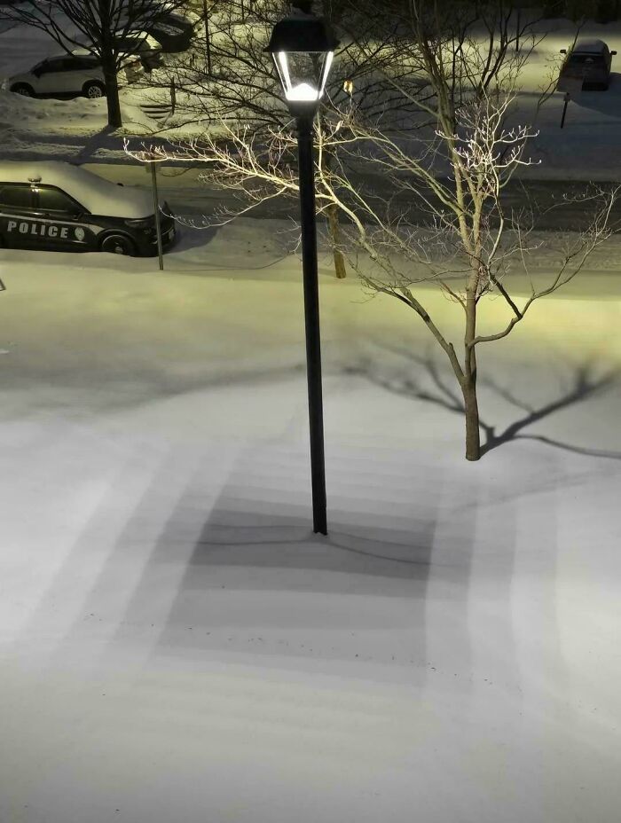 Snow shadows create optical illusion around a streetlamp at night confusing the eye