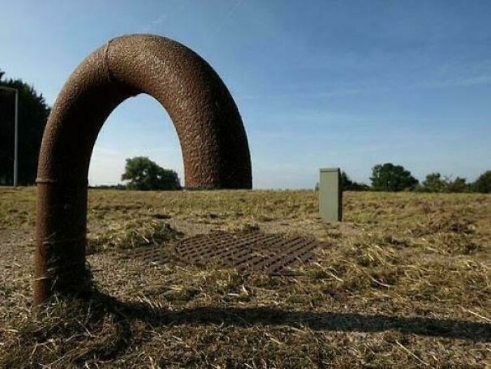Rusty curved pipe on ground looks like a giant loop in an open field