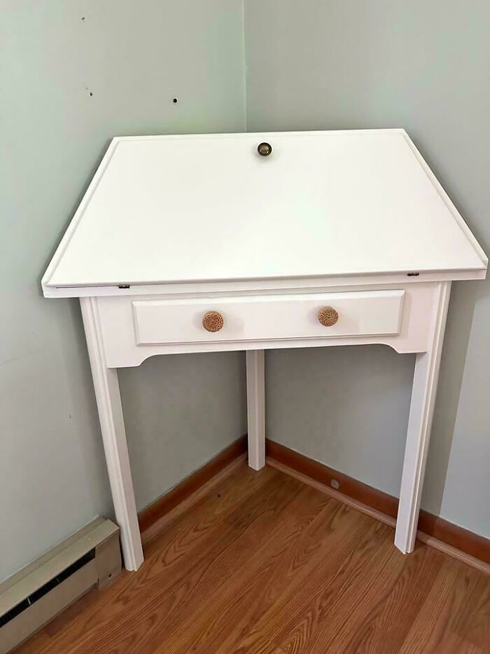 White desk with drawers appears to stand on three legs and a wall corner, confusing the eye