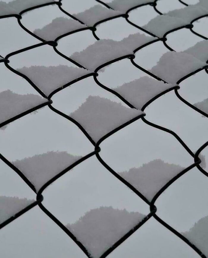 Snow settling in diamond shapes on chain-link fence confusing the eye