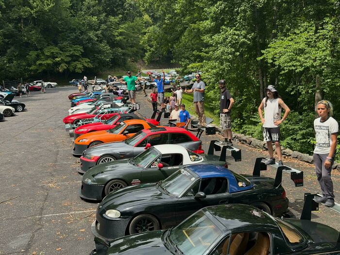 Car meetup with multiple colorful sports cars and people posing on trunks