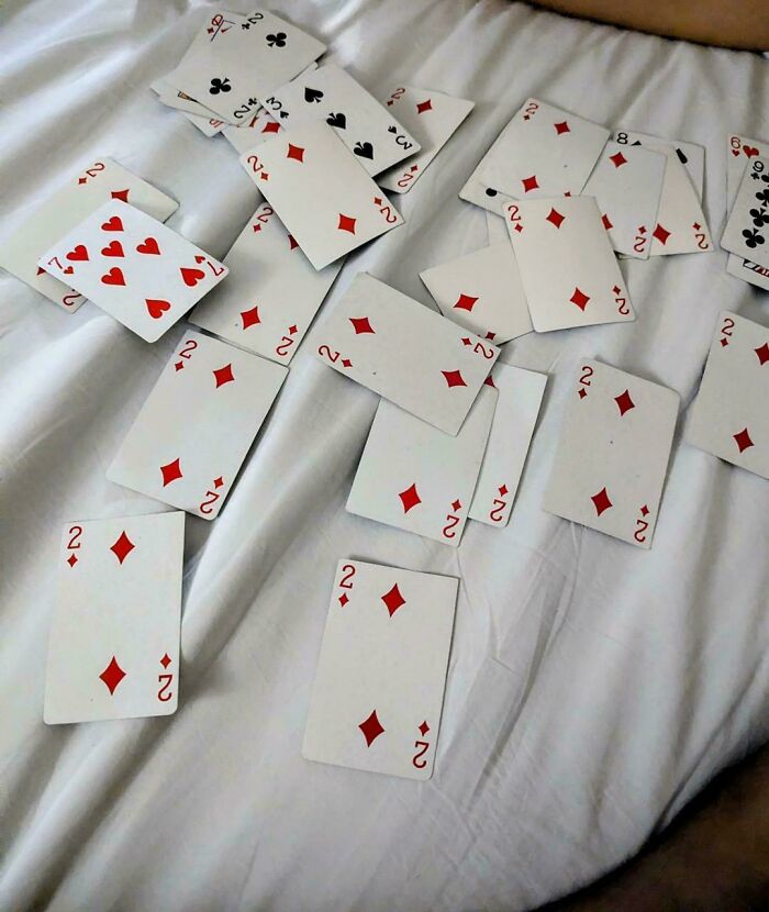A pile of playing cards with mostly number twos facing up on white bedsheets
