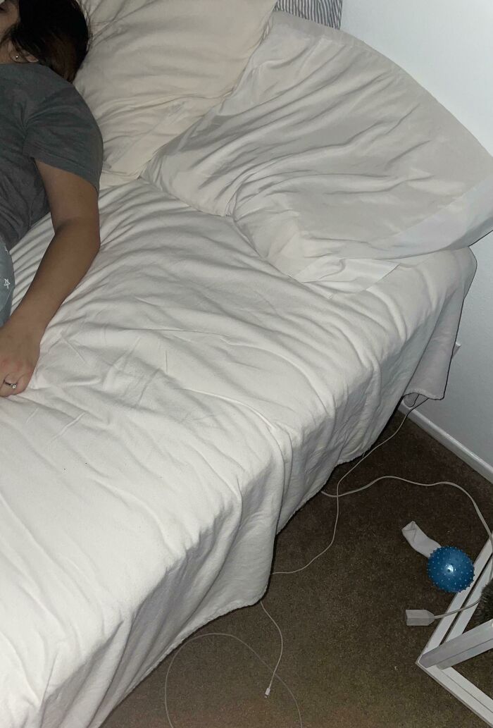 A woman sleeping on the very edge of a large bed, showing unhinged things wives do