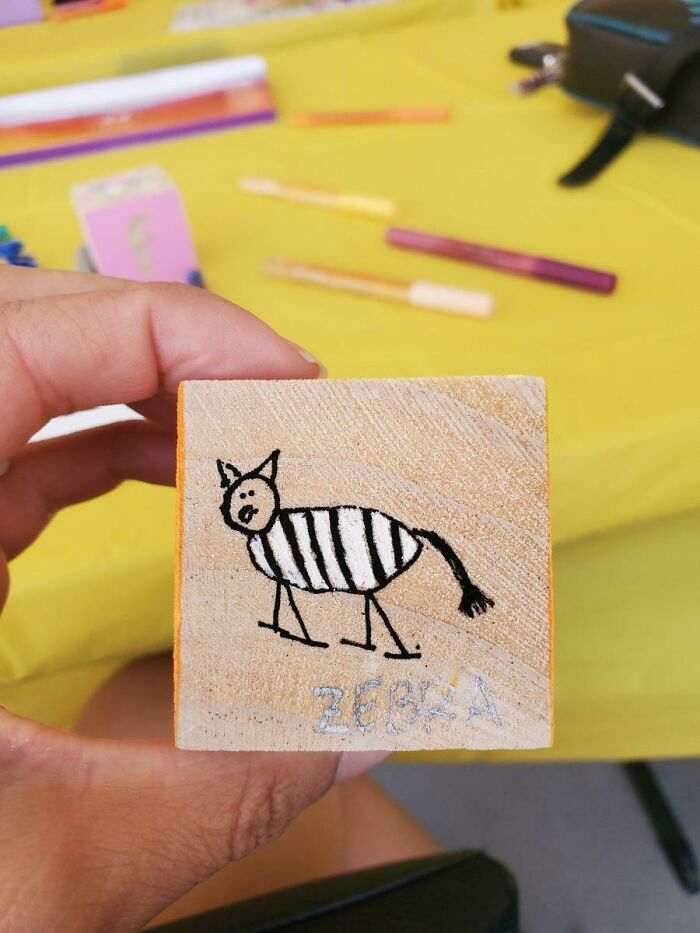 A hand holding a wooden block with a funny zebra child drawing, showing unhinged things wives do