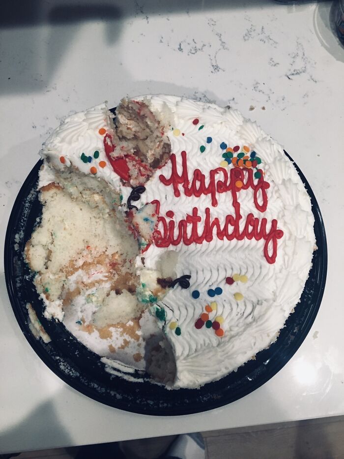A white birthday cake with red lettering where a piece has been eaten directly from the top.