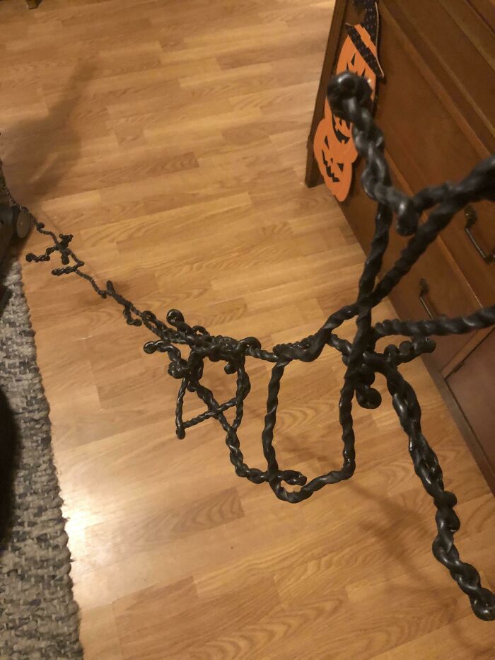 A twisted black metal stand standing on a wooden floor, illustrating unhinged things wives do.