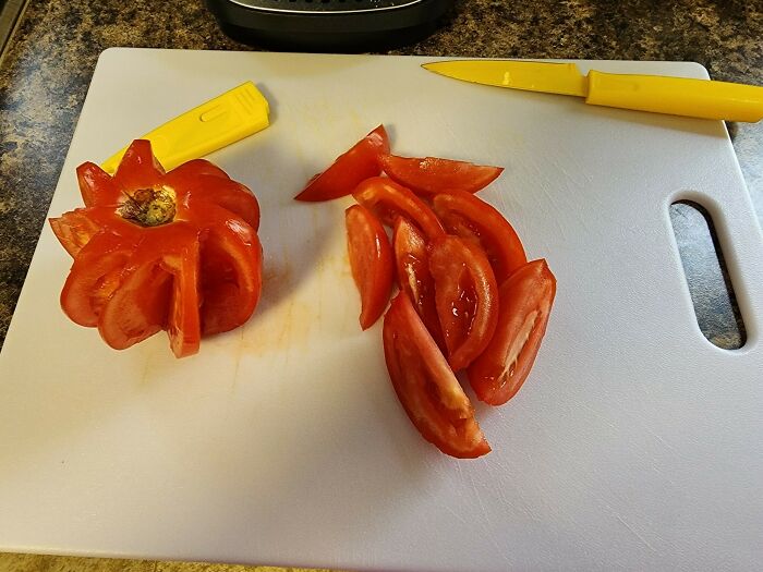 A tomato sliced in a strange pattern on a cutting board, showing unhinged things wives do.