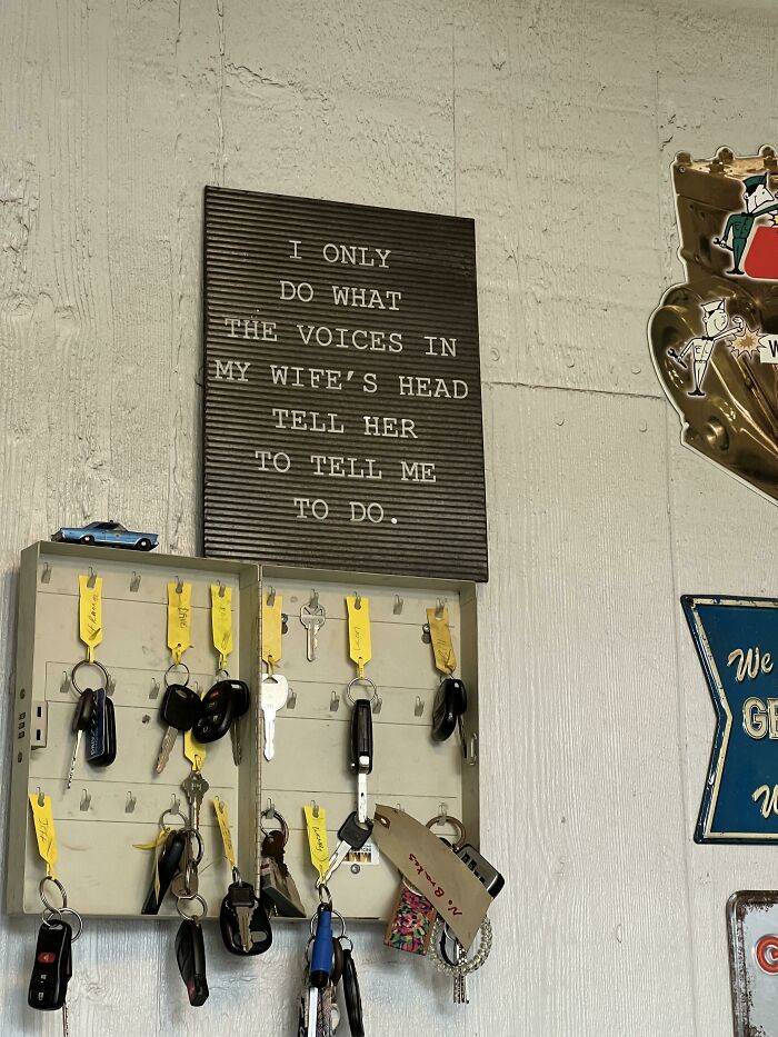 A funny sign about wives above a key rack reading I only do what the voices in my wife's head tell her to