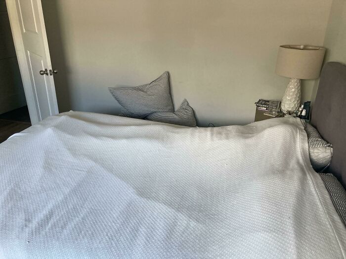 An unmade bed with striped pillows tossed on the floor, showing funny things wives do
