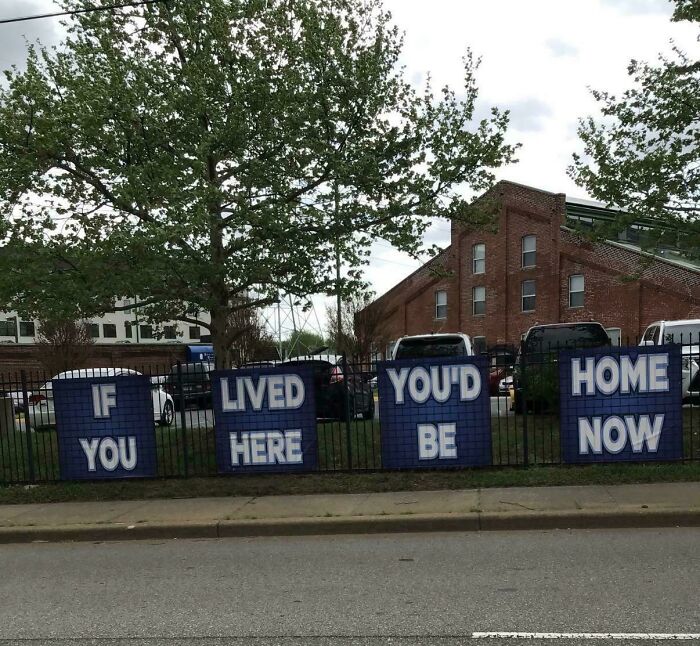 Blue signs on a fence featuring poorly ordered text creating a badly designed sign.
