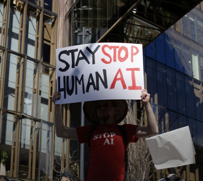 Protester holding a sign with badly designed signs layout reading Stay Human, Stop AI in an awkward order.