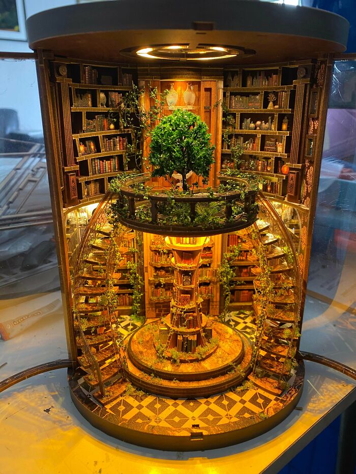 An ornate, illuminated spiral staircase library book nook with a green tree