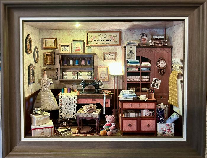 A detailed sewing shop book nook insert featuring miniature fabric, a sewing machine, and a pink teddy bear.