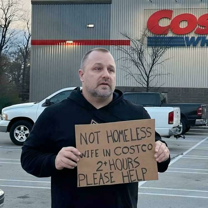 Husband holding a sign in a parking lot about his wife shopping, showing things wives do.