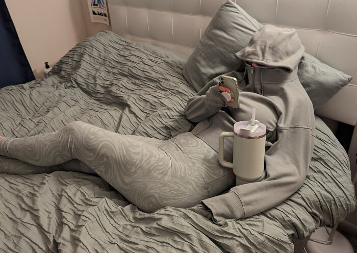 Woman in grey hoodie and leggings using her phone, showing funny things wives do.