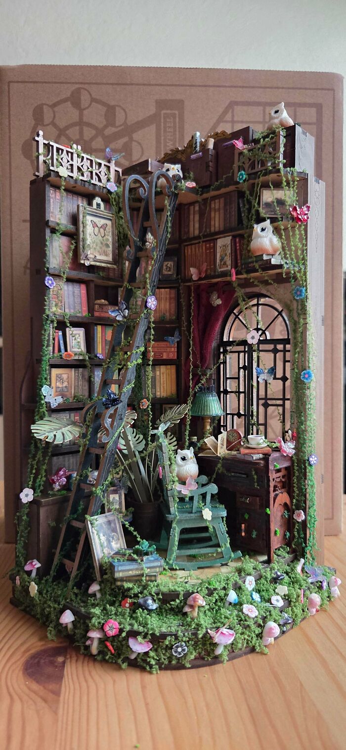 An enchanted library book nook covered in vines, featuring miniature owls and a rocking chair