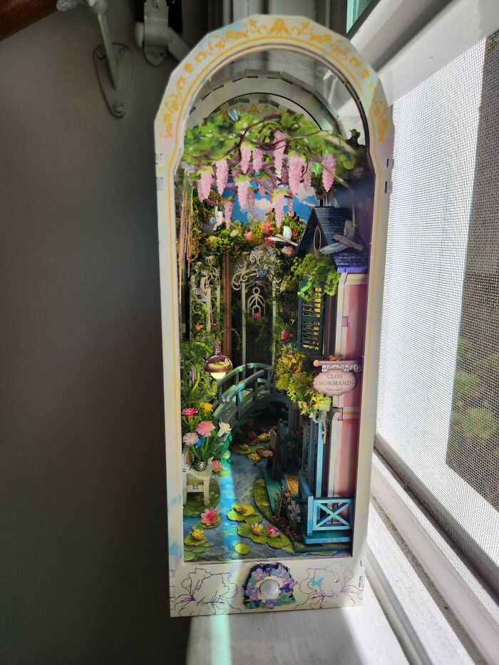 A magical garden path book nook with a bridge and hanging flowers on a windowsill