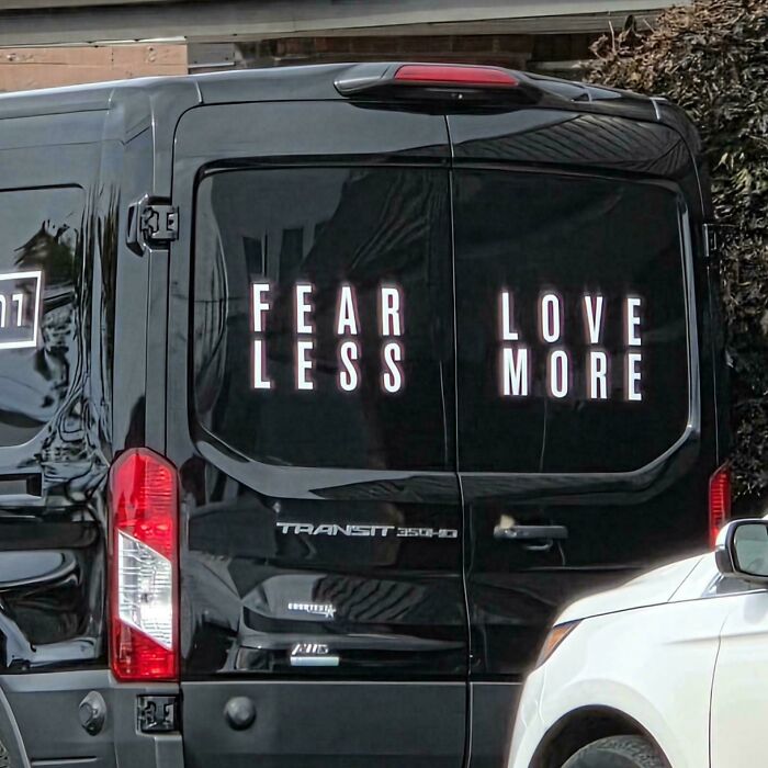 Black van doors showing badly designed signs split in half, reading FEAR LESS LOVE MORE in a confusing layout.