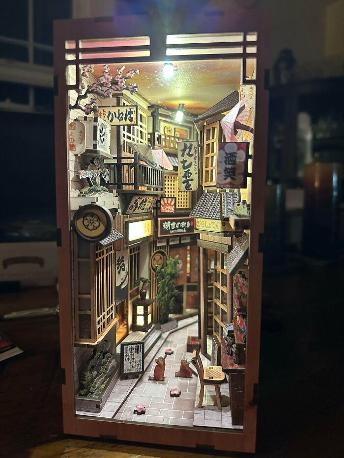 A Japanese style book nook featuring a miniature alleyway at night with glowing signs and tiny cats
