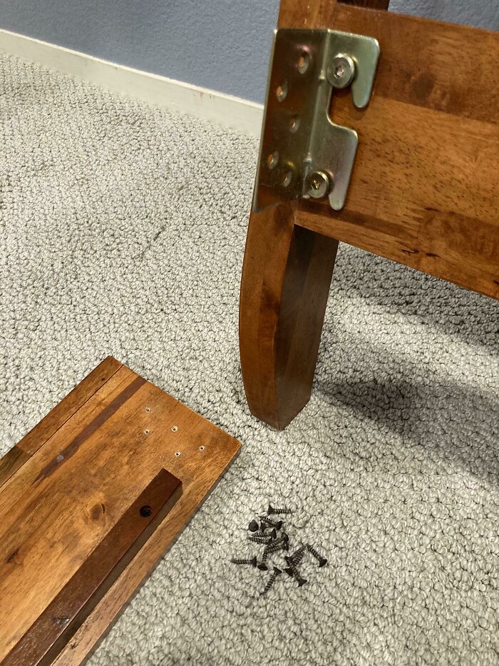 Unassembled wooden furniture parts and screws on carpet, showing funny things wives do