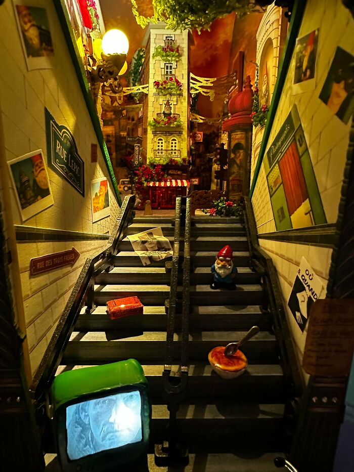 A detailed book nook miniature of a Parisian street with stairs, a tiny gnome, and a mini TV screen