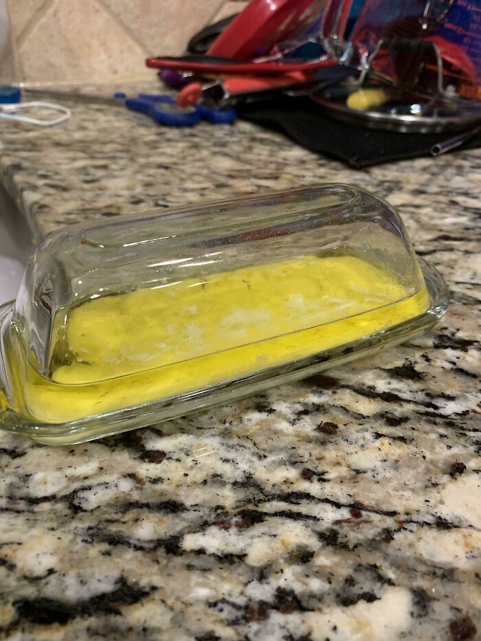 A stick of butter melted in a glass dish on a counter, showing funny things wives do