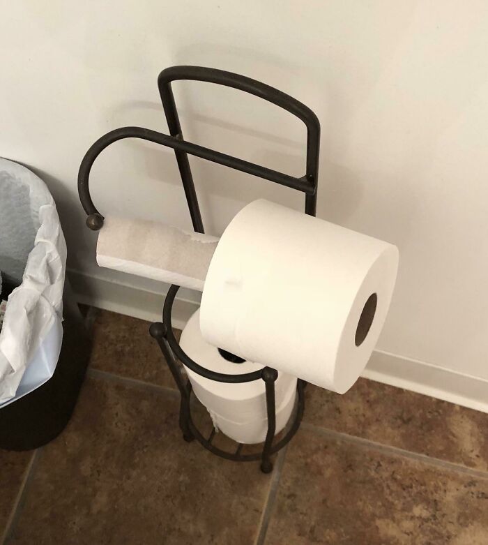 A toilet paper roll placed awkwardly on the holder instead of through the tube.