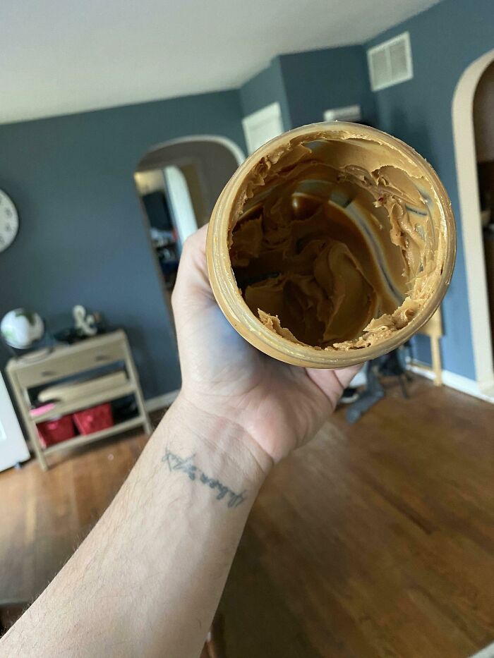 A hand holding an almost empty jar of peanut butter, showing one of the funny things wives do.