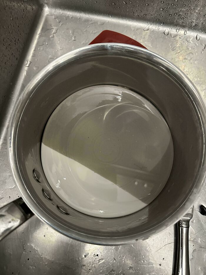 A white plate perfectly stuck at the bottom of a metal pot, illustrating annoying things wives do.