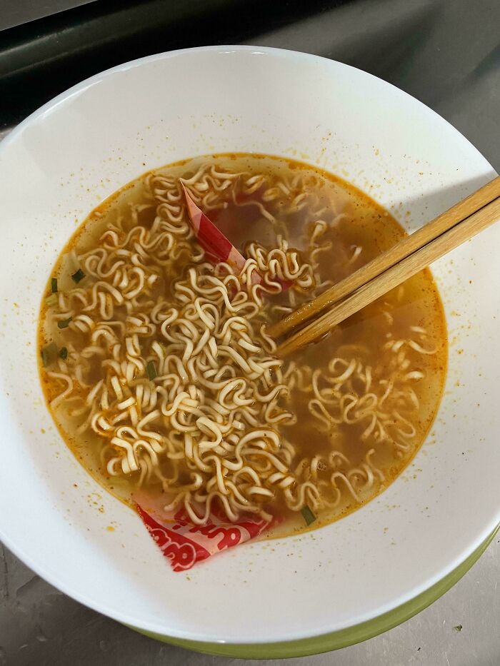 A white bowl of instant ramen with seasoning packets left inside, illustrating unhinged things wives do.