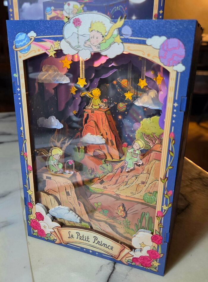 A whimsical Le Petit Prince themed book nook with three-dimensional cutout characters, stars, and planets.