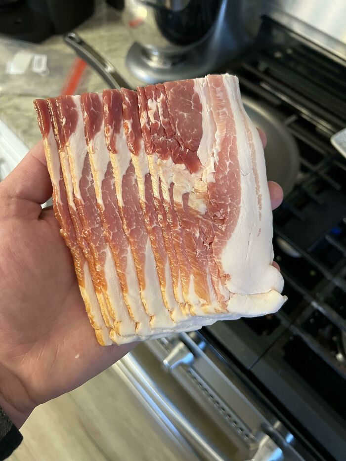 A hand holding a block of uncut bacon, illustrating funny things wives do