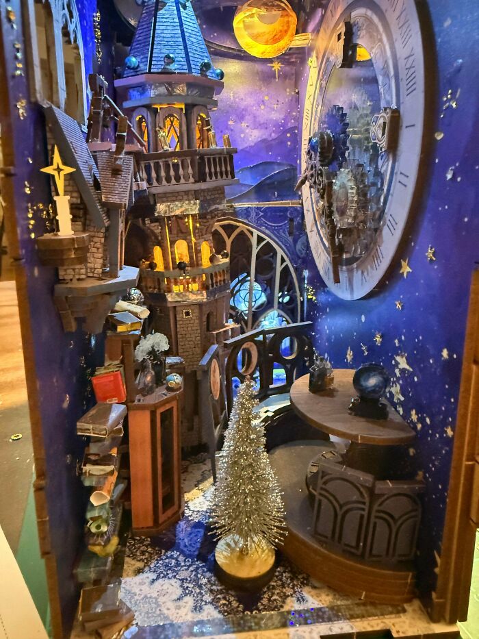 A magical wizard tower book nook lit up with starry skies, a clock face, and a tiny tree.