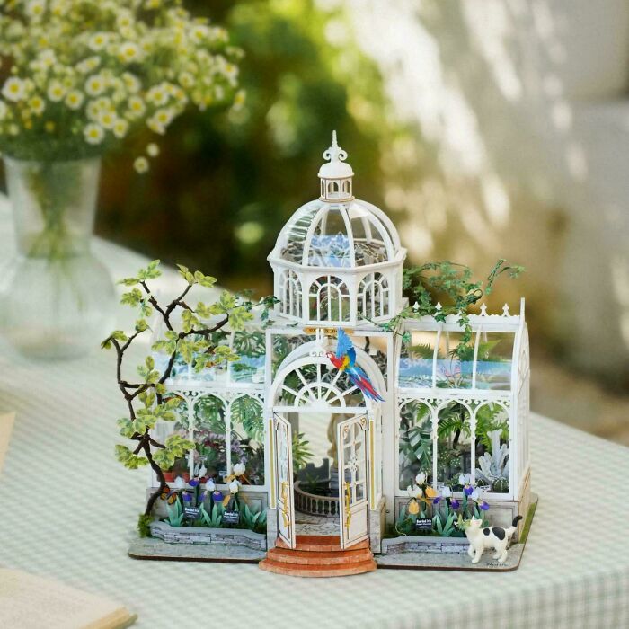 A delicate white conservatory greenhouse miniature kit with paper plants and a small parrot.