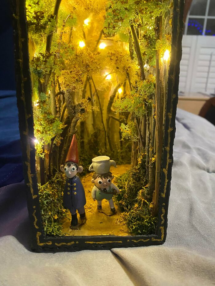 An whimsical book nook showing miniature characters walking through a glowing autumn forest