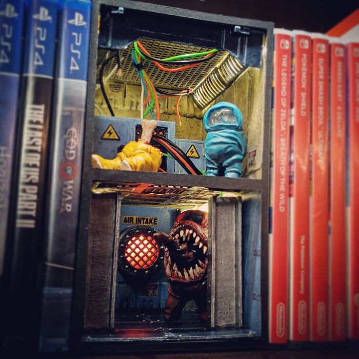 An Among Us themed book nook featuring game characters and an air intake vent, placed between game cases.