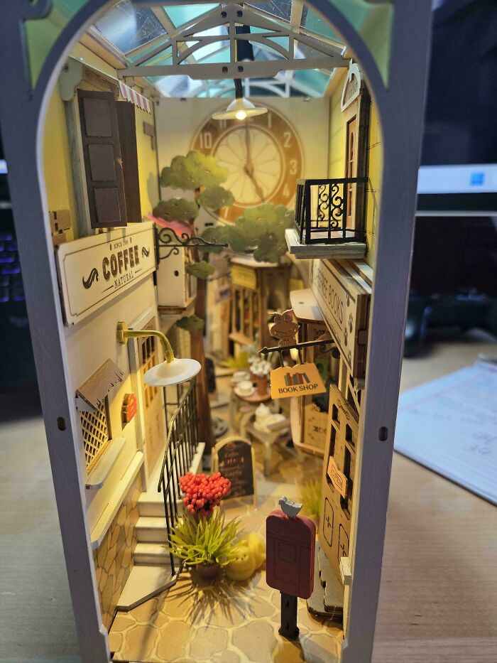 Side view of a miniature book nook depicting a quaint European street with a coffee shop and clock.