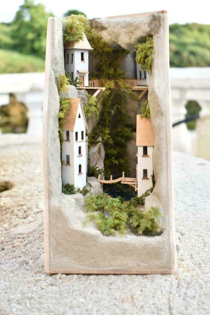 An artistic, nature-inspired book nook depicting a tiny village with white houses built into a mossy cliffside.