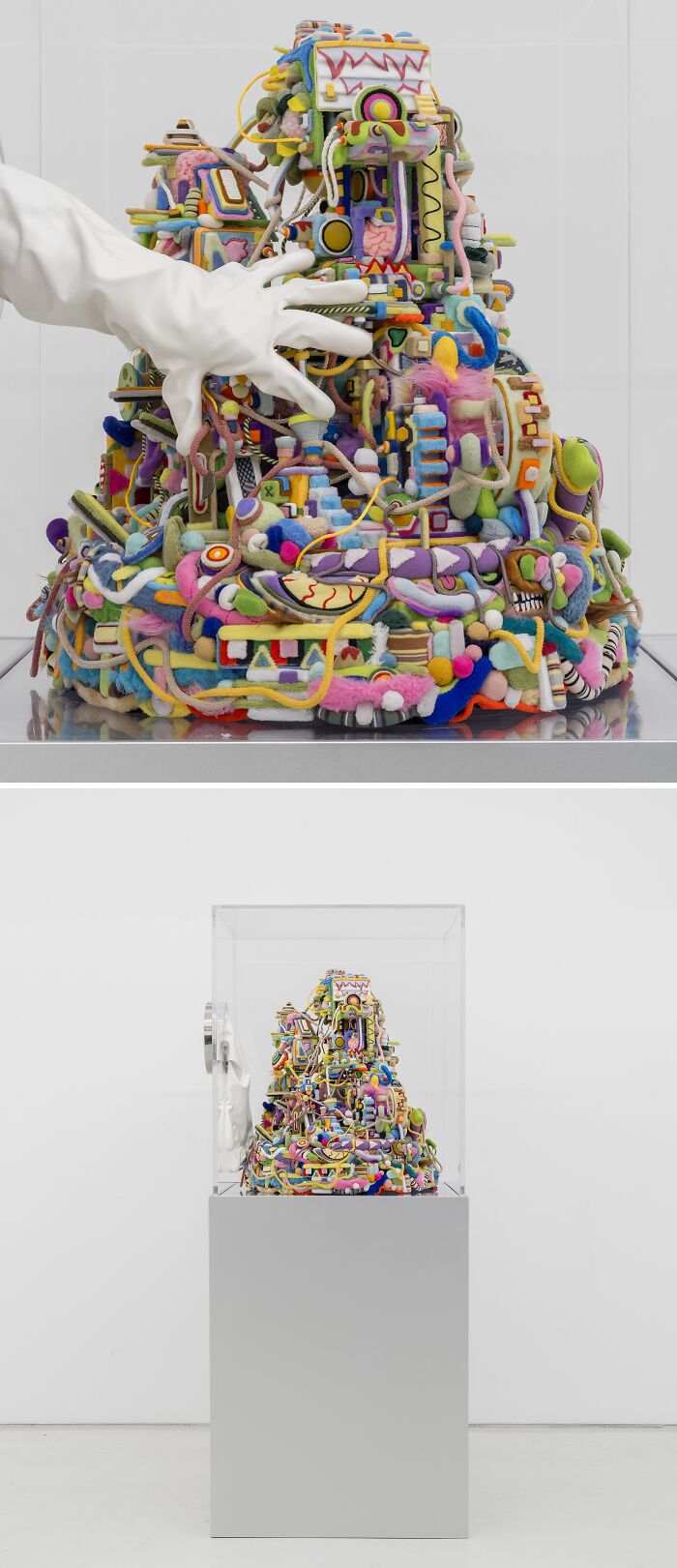 A hand wearing a white glove touching a colorful, chaotic, textured mound of unusual sculptures