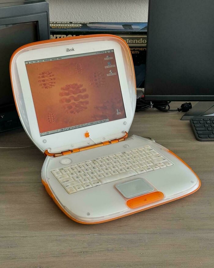 A retro orange Apple iBook G3 clamshell laptop open on a wooden desk.
