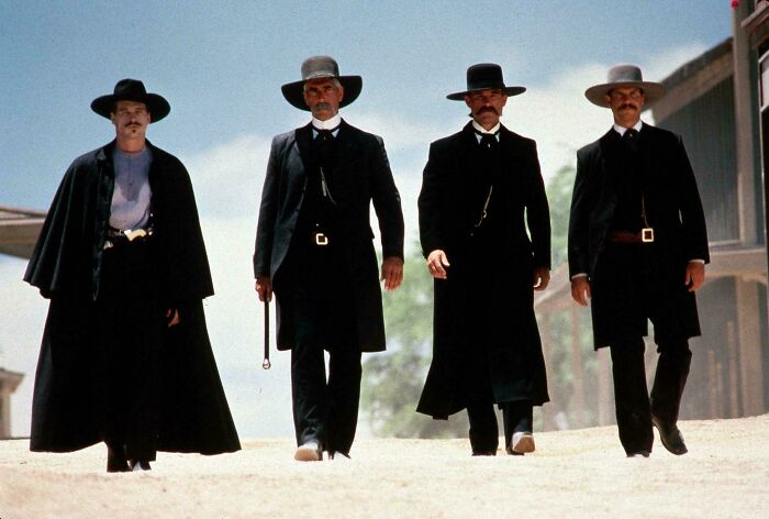 Four cowboys from the '90s movie Tombstone walking side by side on a dirt road