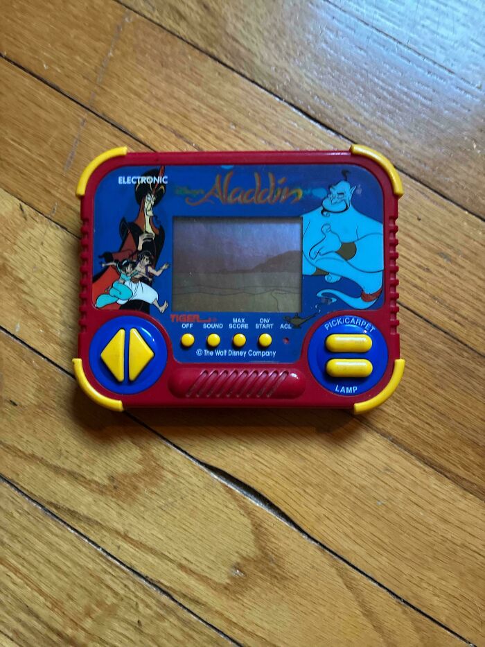 An old Tiger Electronics Aladdin handheld game on a wooden floor, a symbol of the 90s.