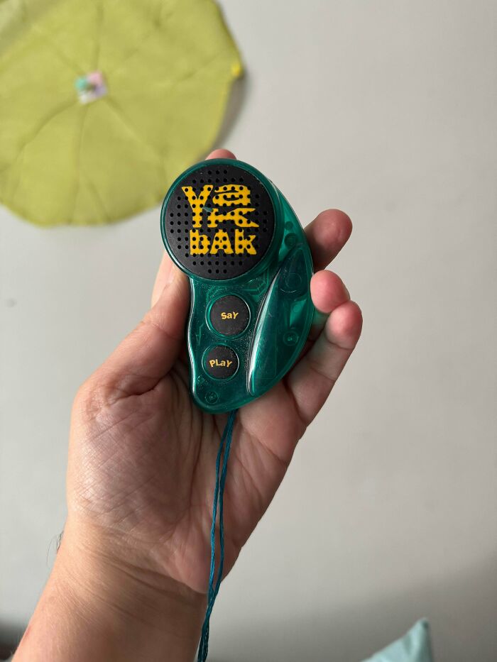 A hand holding a green translucent Yak Bak voice recorder toy, a popular gadget from the '90s.