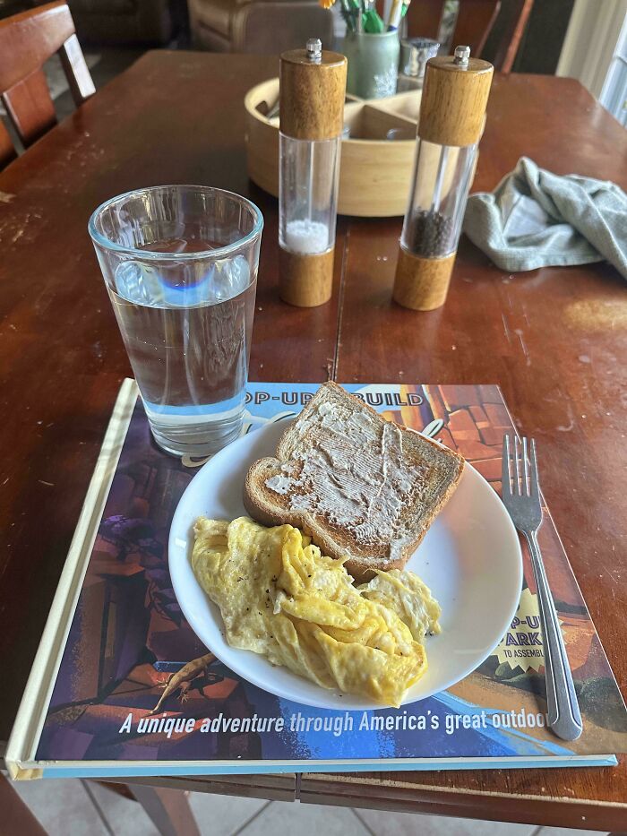 A plate of eggs and toast served on a book with a glass of water, illustrating wholesome pics of dads caring for family.