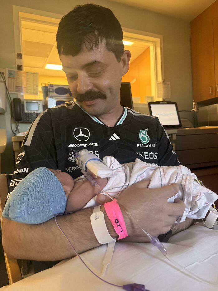 A proud dad with a mustache holding his newborn baby in a hospital room, capturing wholesome pics of dads